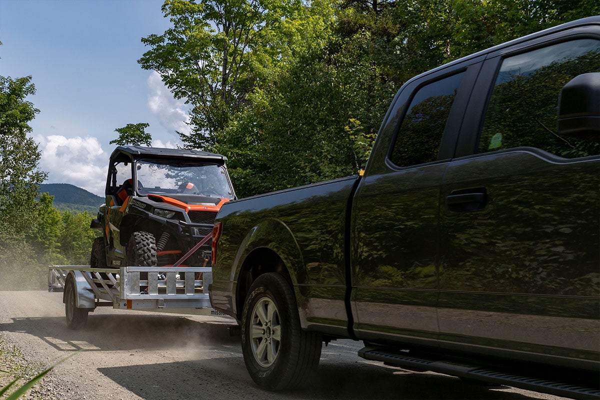 Open aluminum ATV / UTV trailer from ALCOM, pulling a side by side behind a truck
