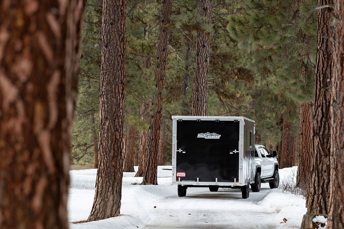 Truck towing an aluminum All-Sport trailer through the trees in Montana