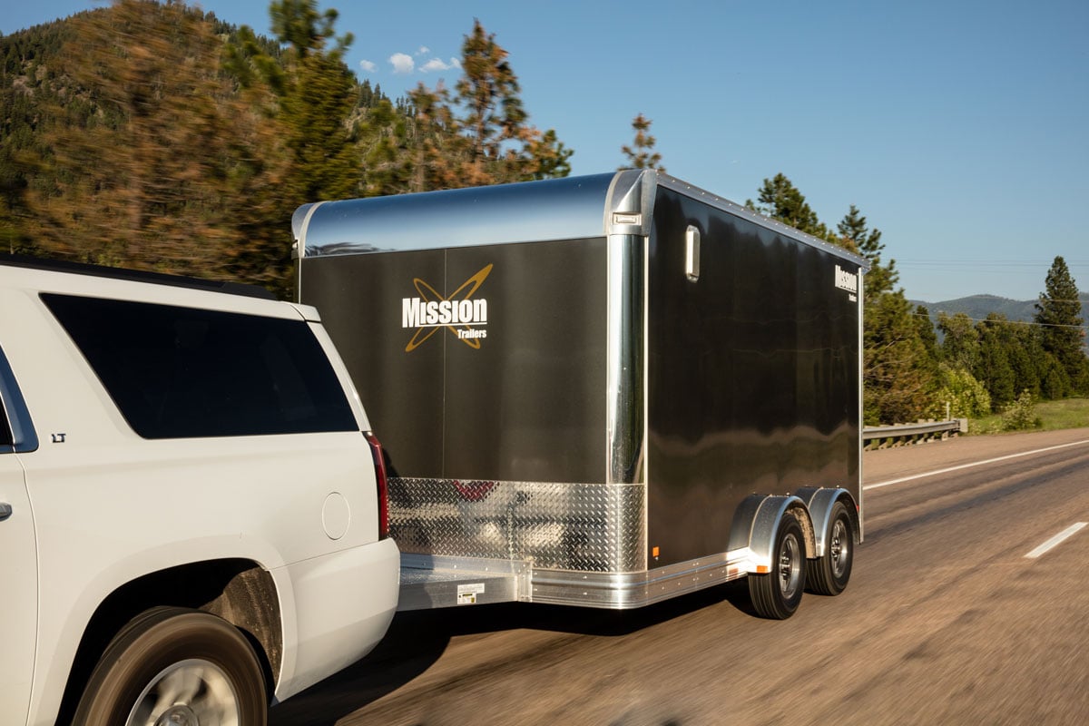 Enclosed aluminum side-by-side trailer towed by a white SUV
