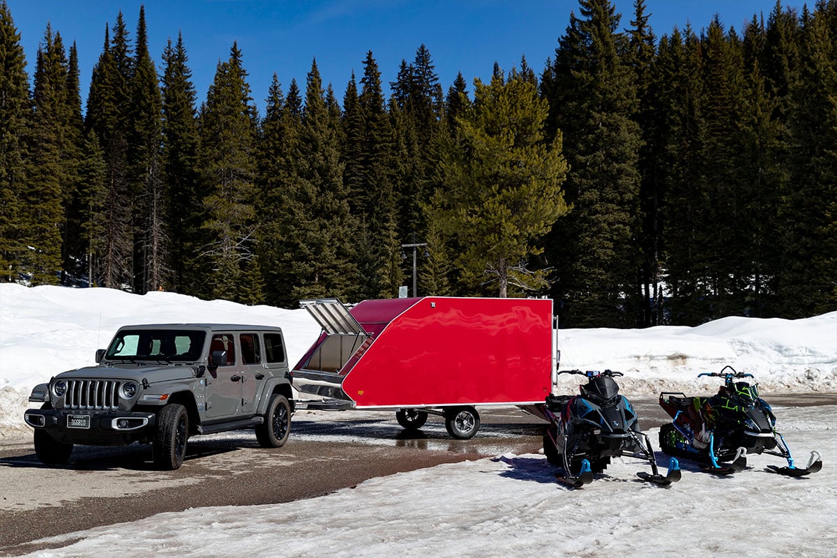 Red aluminum Crossover snow trailer hitched to a Jeep in late winter