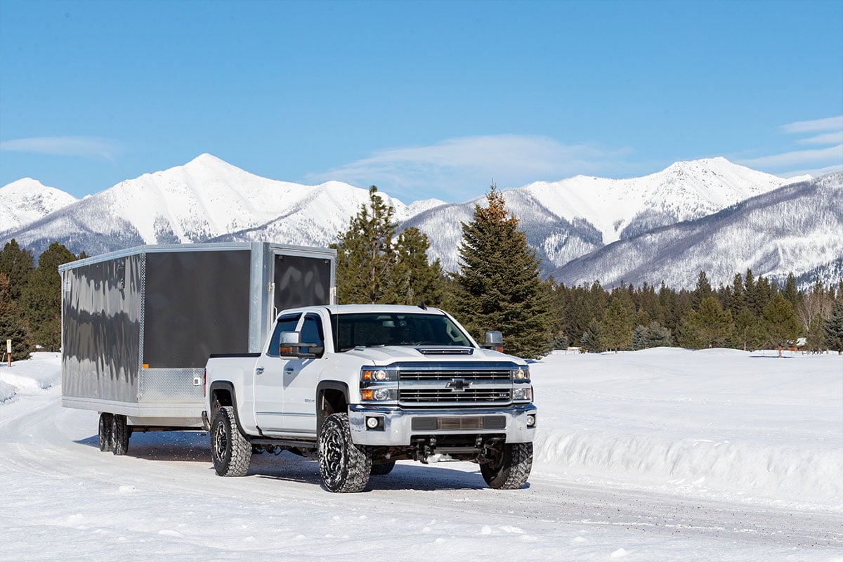 Gray enclosed deckover snowmobile trailer towed on a snowy Montana road