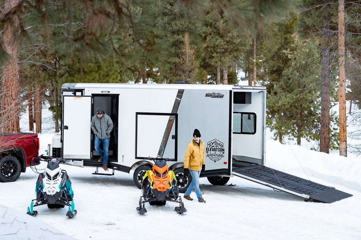 Snowmobiles unloaded from a parked Elevation Series enclosed snowmobile trailer