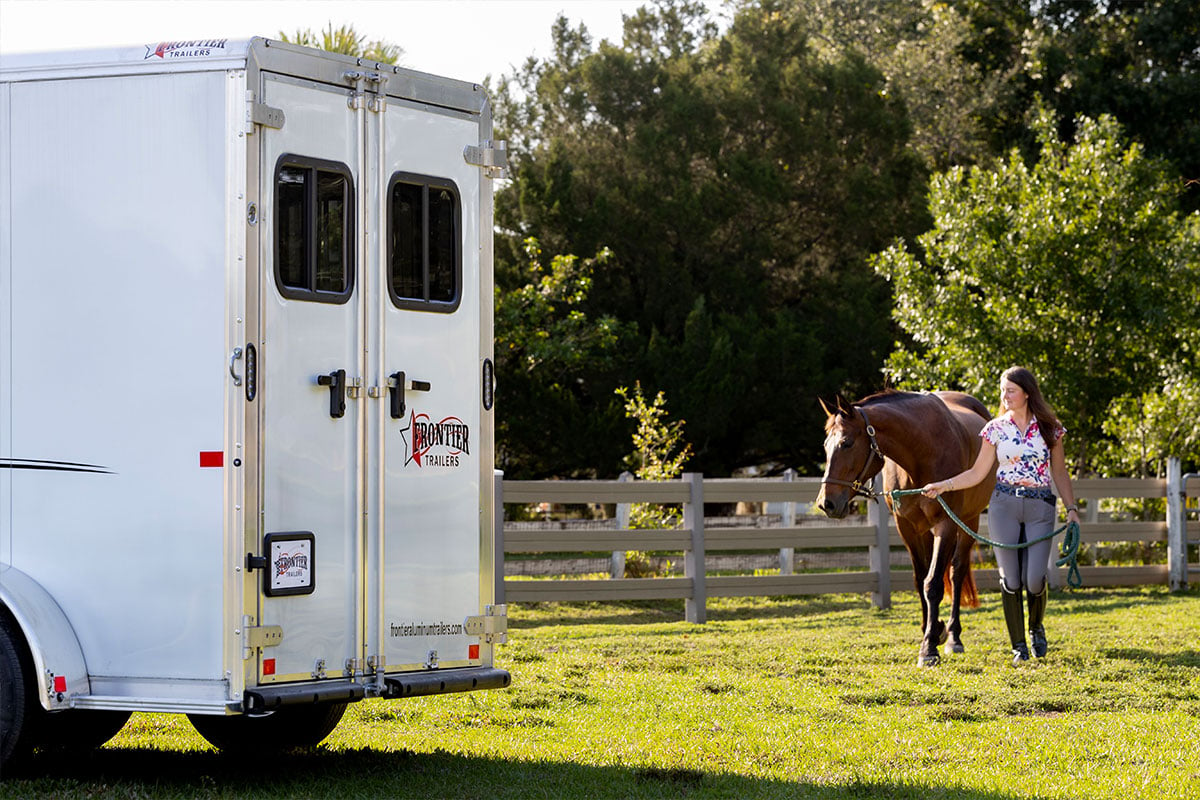 Frontier horse trailer parked in a field with a horse and rider walking