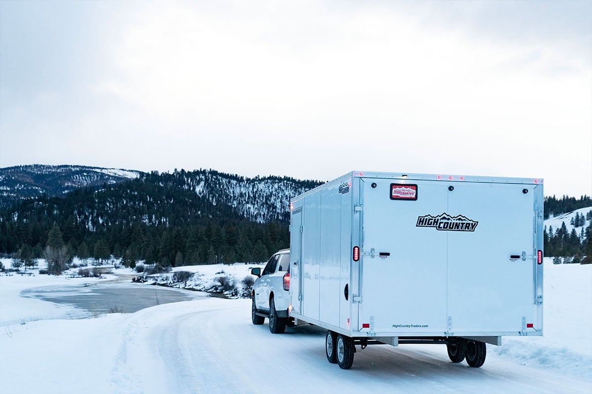 Enclosed aluminum snowmobile trailer by High Country, an ALCOM brand, on a snowy road in the mountains