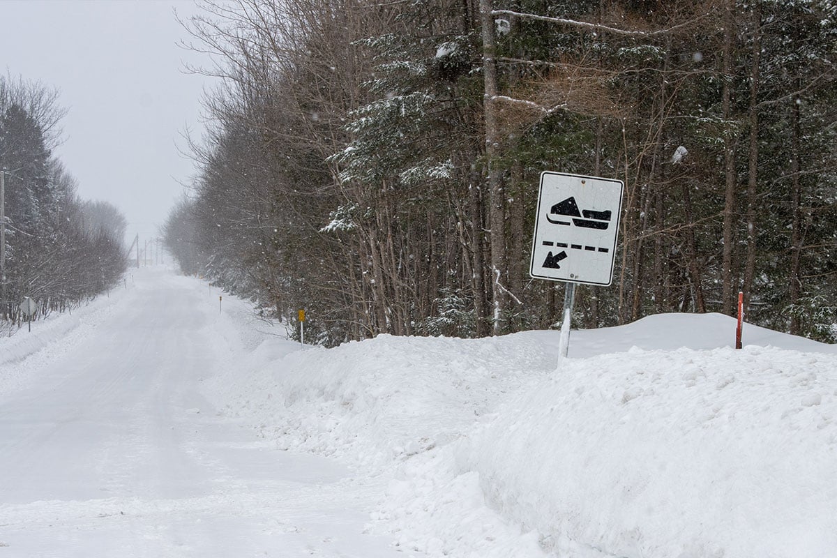 Roadside sign directing snowmobile riders to the Great Canadian Snowmobile Trail in deep snow.
