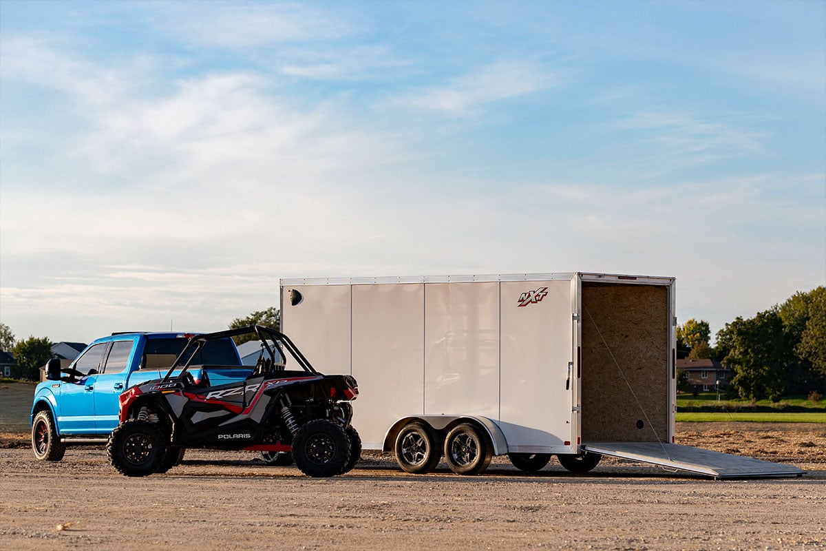 Enclosed white aluminum UTV trailer with RZR side by side parked beside it.