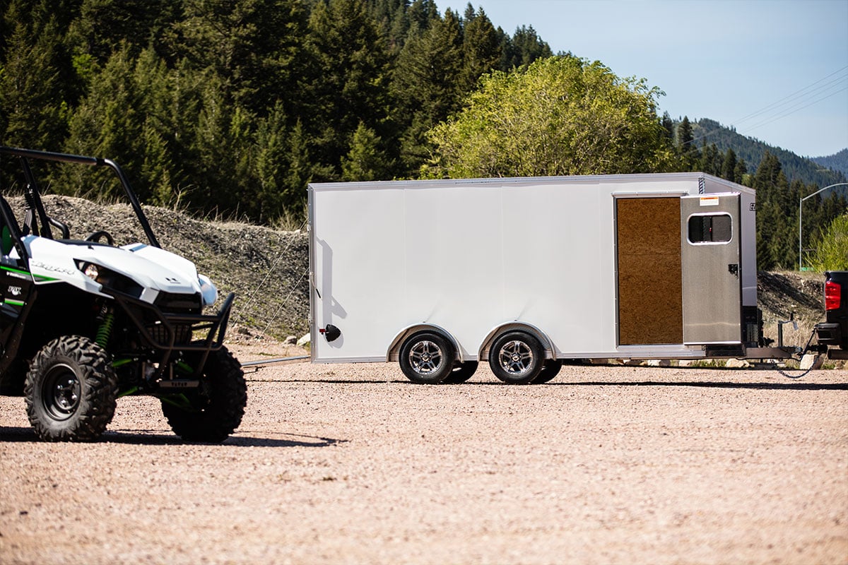 A white aluminum enclosed UTV trailer with side access door; UTV in foreground