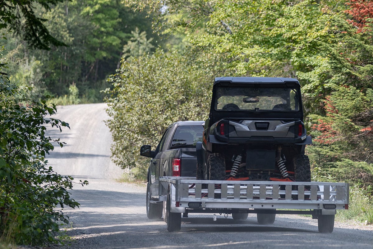 Pickup truck towing open ALCOM aluminum UTV trailer on a back road
