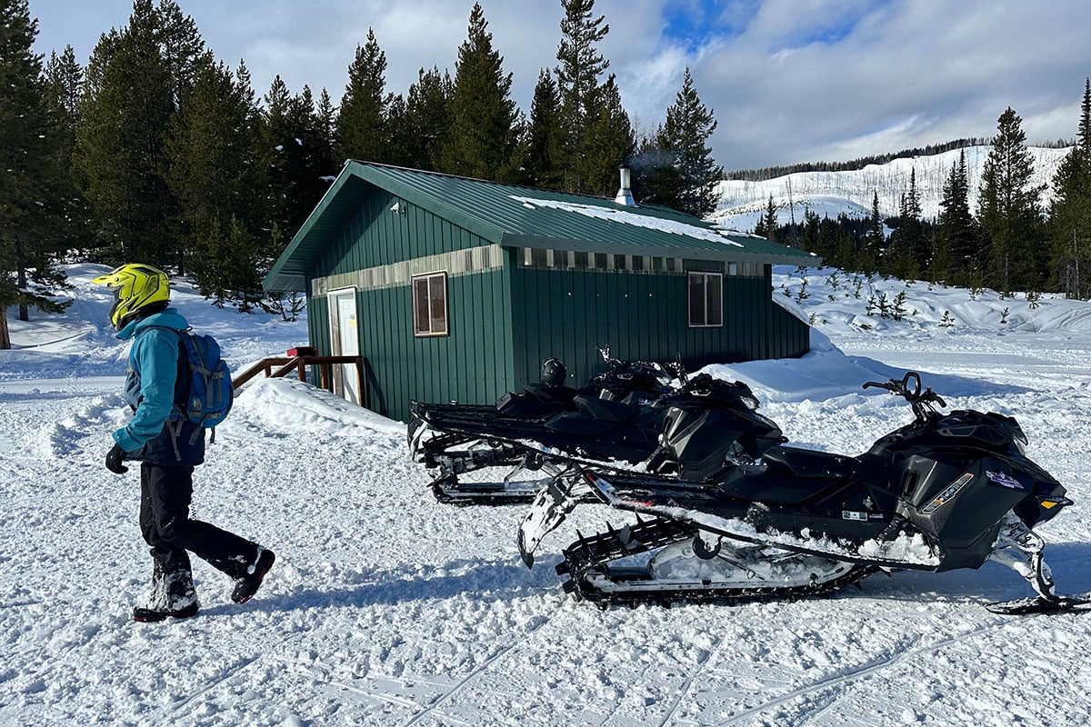 Snowmobile parked by a shed, rider walking on the snow in Seeley Lake, MT