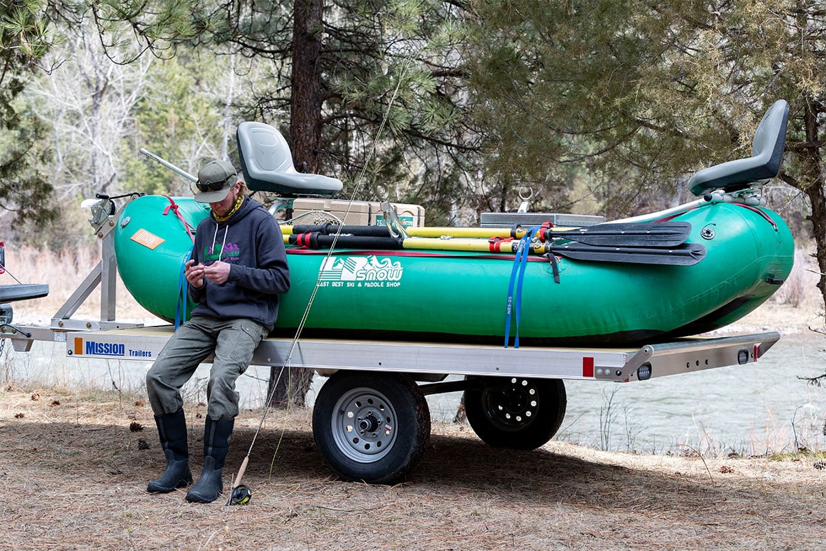 An angler getting ready to go raft fishing; raft is secured to an ALCOM aluminum trailer.