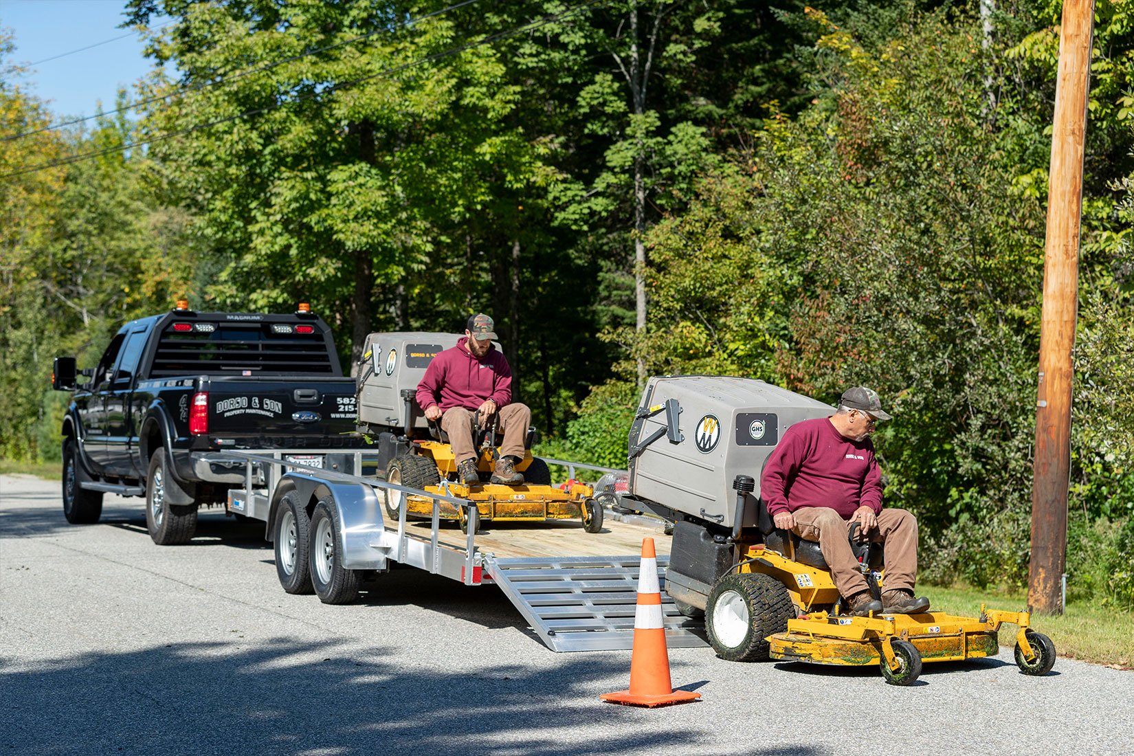 Driving lawn mowers off an ALCOM wood deck aluminum landscape trailer