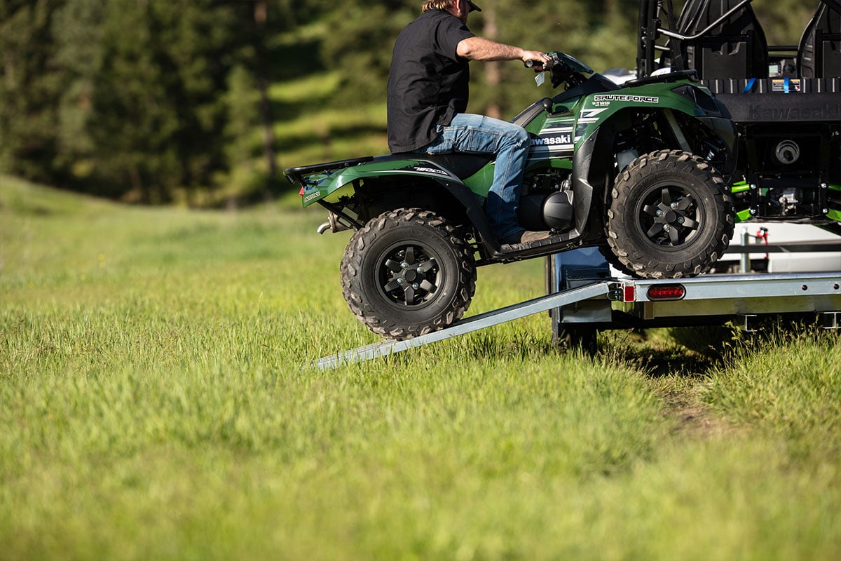 Driving an ATV onto an open aluminum ALCOM trailer using stowaway ramps.