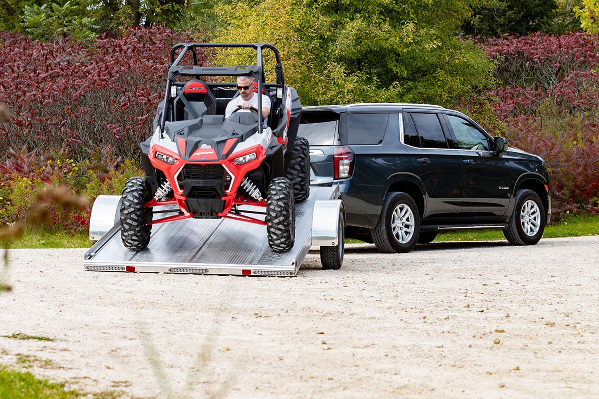 Man driving an ATV off an open ALCOM tilting aluminum trailer.