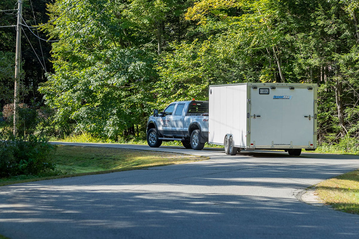 An enclosed aluminum car trailer from ALCOM being towed by a pickup truck