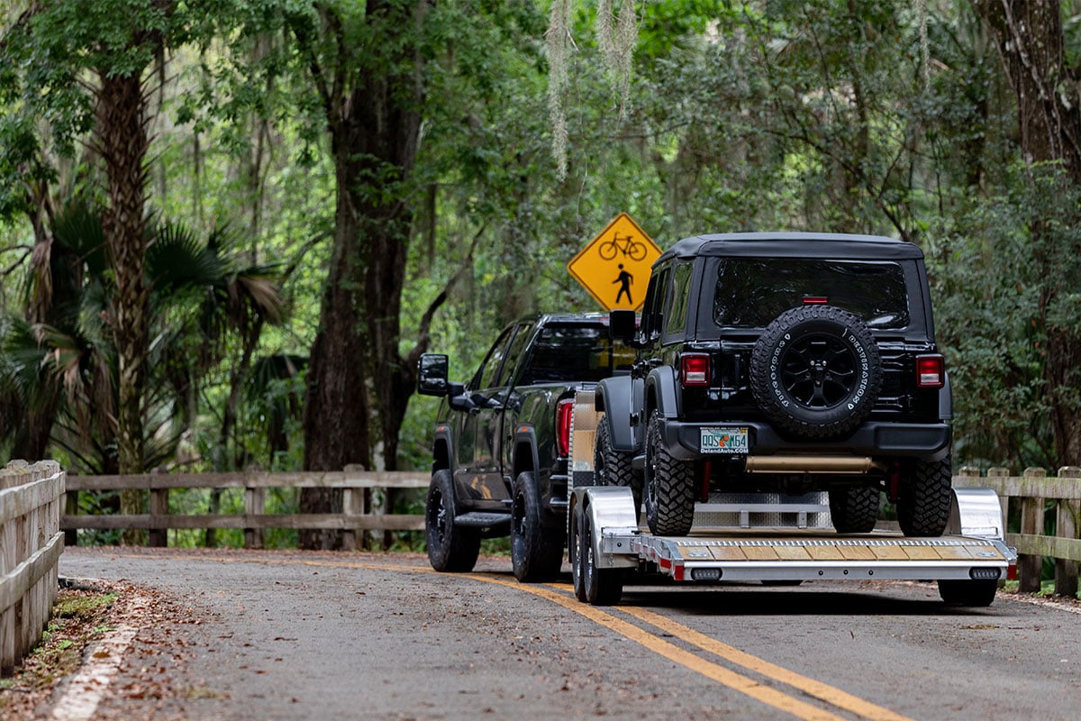Open wood deck aluminum car trailer by ALCOM loaded with a Jeep