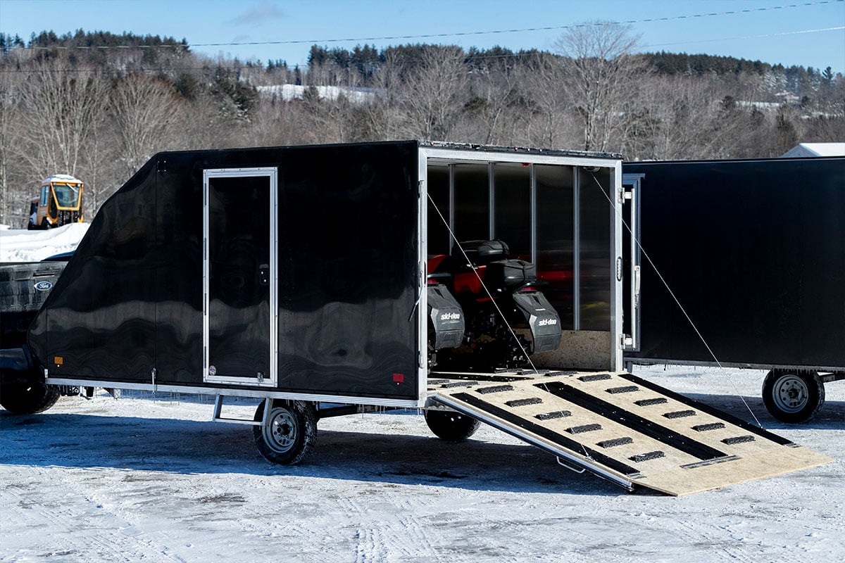 Crossover snowmobile trailer by ALCOM loaded with two sleds, rear ramp door open