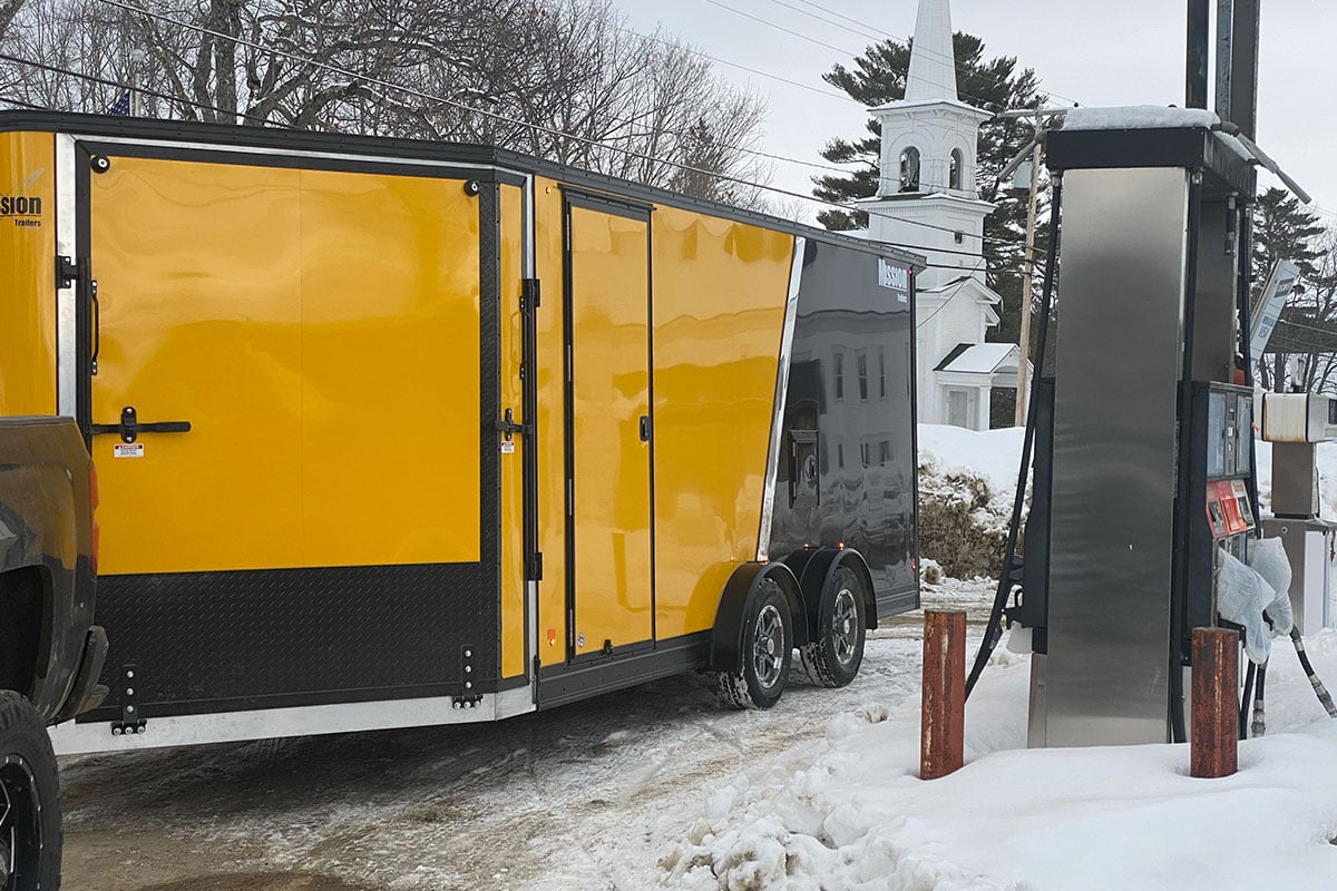 A yellow and black Inline snow trailer at a gas pump