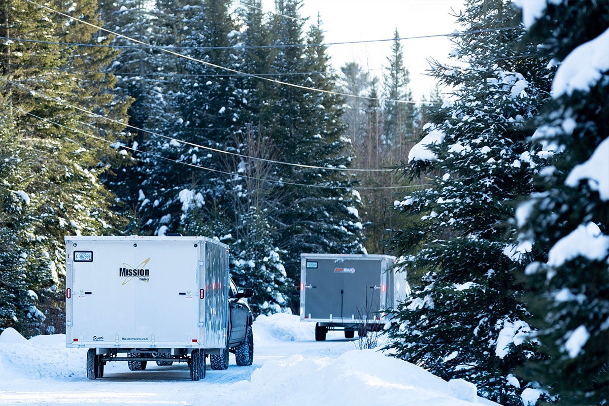 Two ALCOM enclosed snowmobile trailers on the road in winter