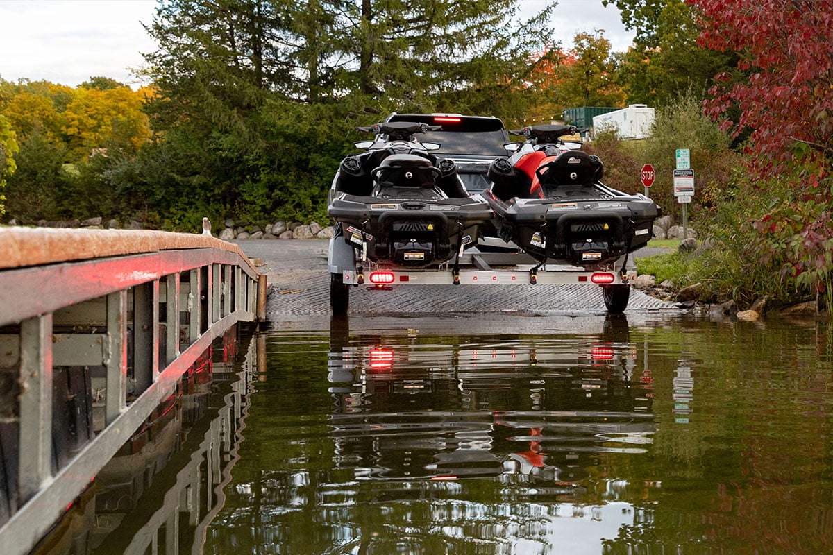 Personal watercraft trailer with two PWCs backing into a launch ramp at the lake
