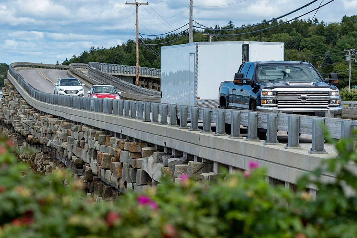 Enclosed aluminum cargo trailer towed by a pickup truck on a bridge in Maine.