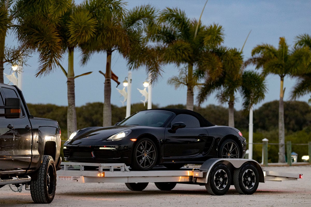 Open car hauler loaded with a sports car parked in front of palm trees.