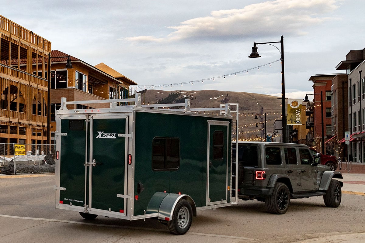 Enclosed cargo trailer with side access door and window towed behind a dark grey Jeep.