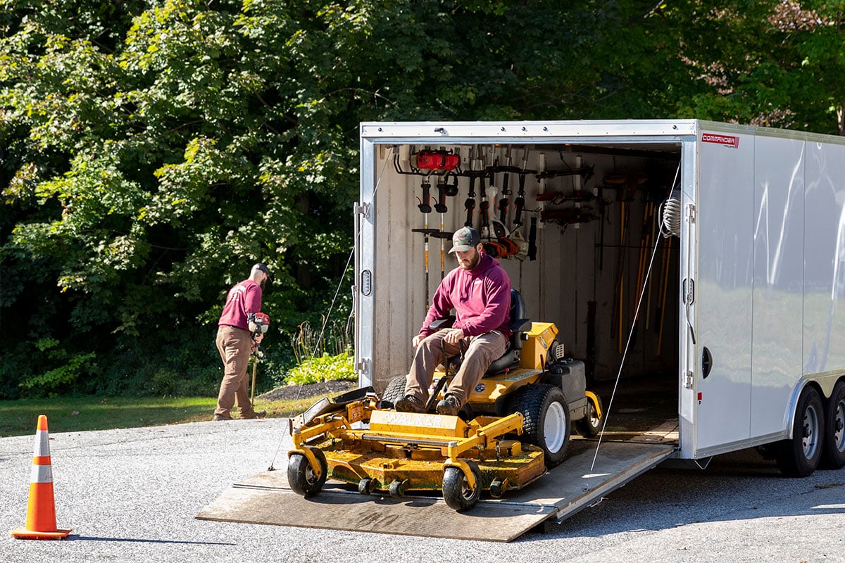 Spring assisted rear ramp door open to allow a riding lawnmower to be driven out of an ALCOM enclosed trailer