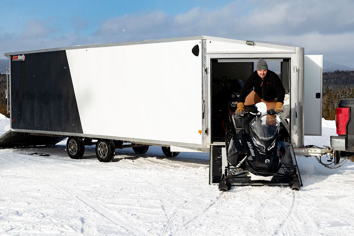 Enclosed deckover snow trailer with front ramp door open and snowmobiler driving out