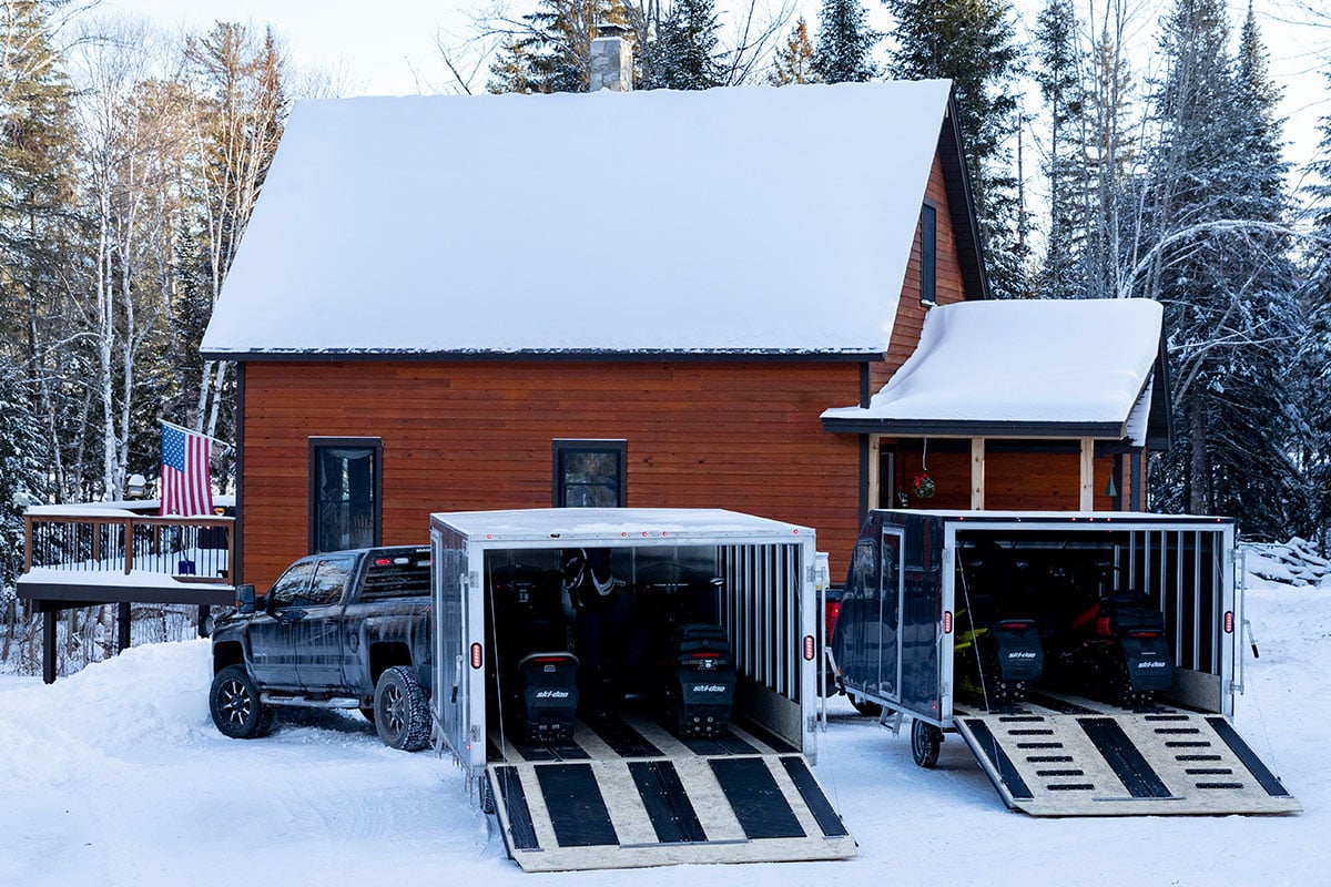 Two enclosed ALCOM snowmobile trailers with rear ramp doors open showing track mats