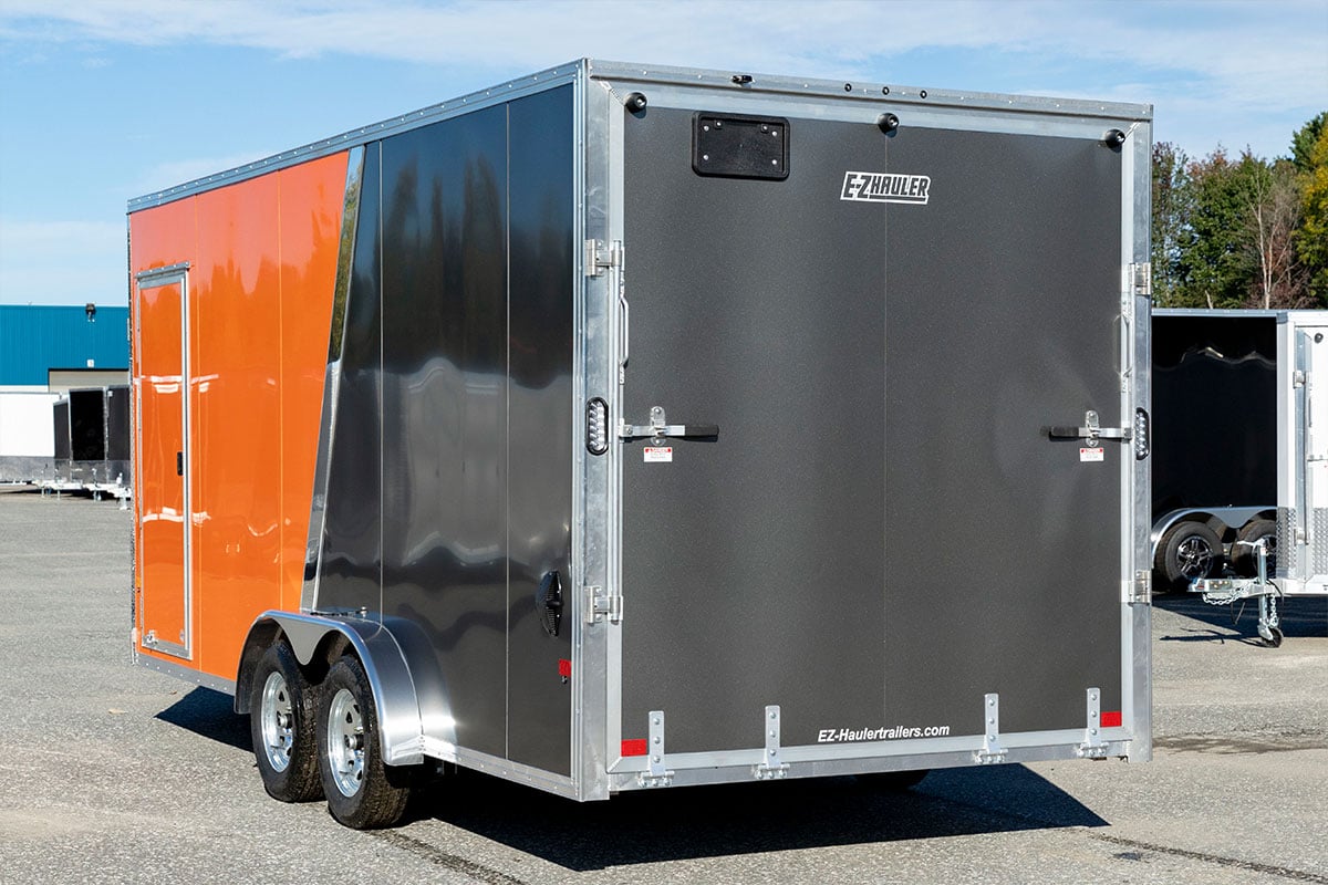 Exterior view of an enclosed aluminum ALCOM trailer showing tires.