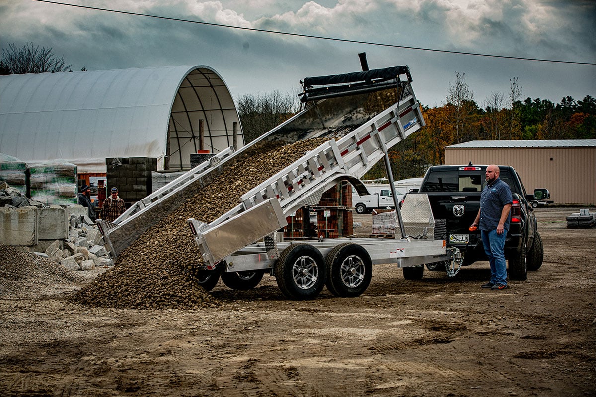 ALCOM commercial dump trailer unloading crushed rock at a jobsite