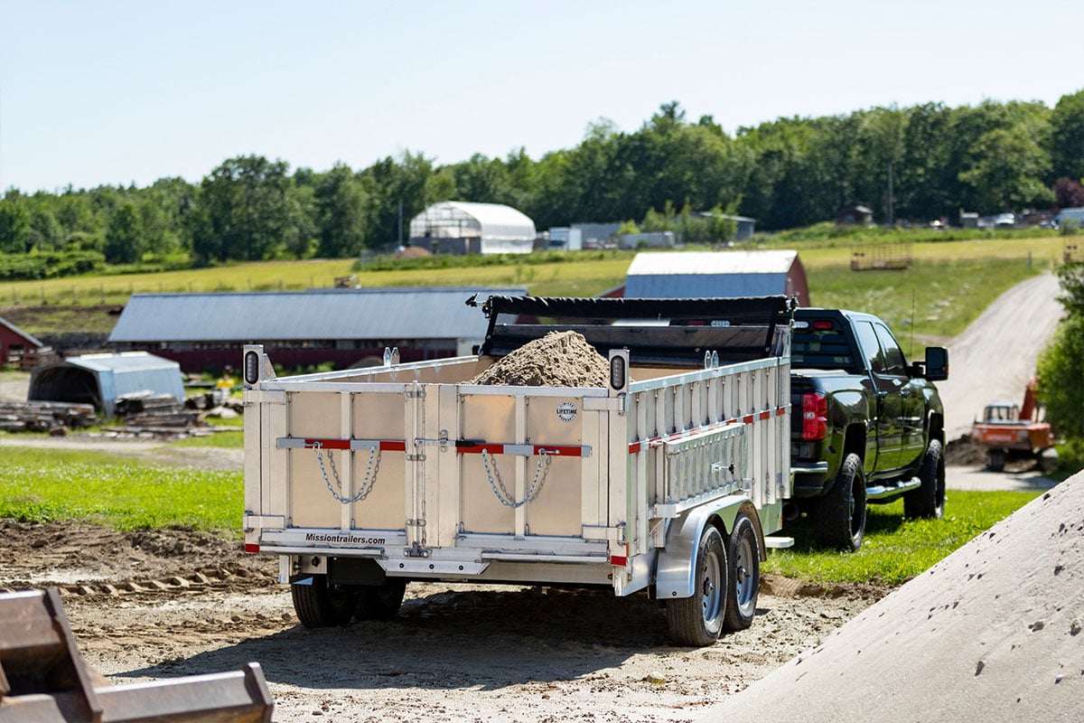 Pickup truck towing a load of dirt in an ALCOM commercial dump trailer. 