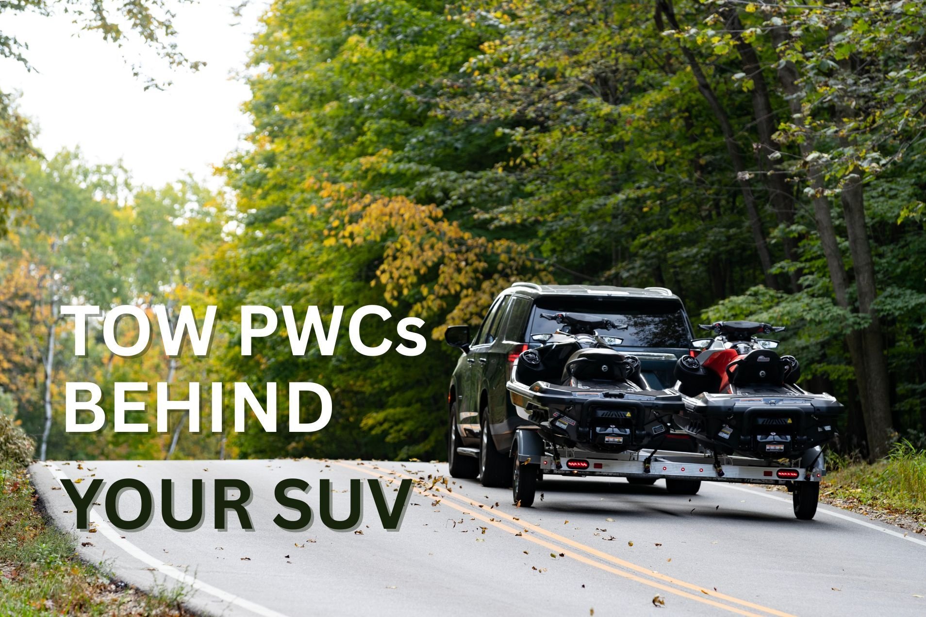 A gray SUV towing a Triton 2-place aluminum PWC trailer on a hilly road lined with green trees