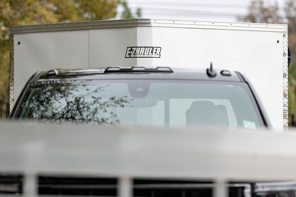 Front view of an enclosed aluminum cargo trailer from EZ Hauler, towed behind a pickup truck.