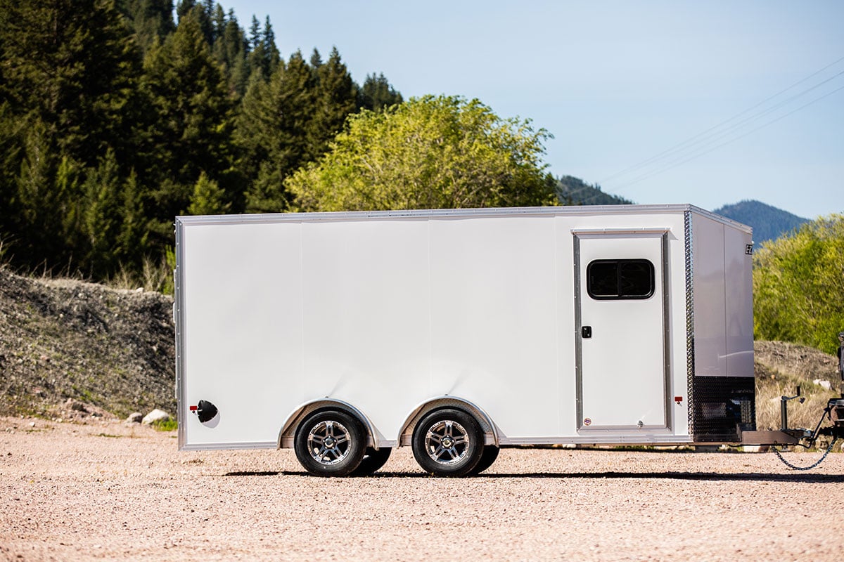 Enclosed white aluminum cargo trailer with side access door parked outside; full side view.
