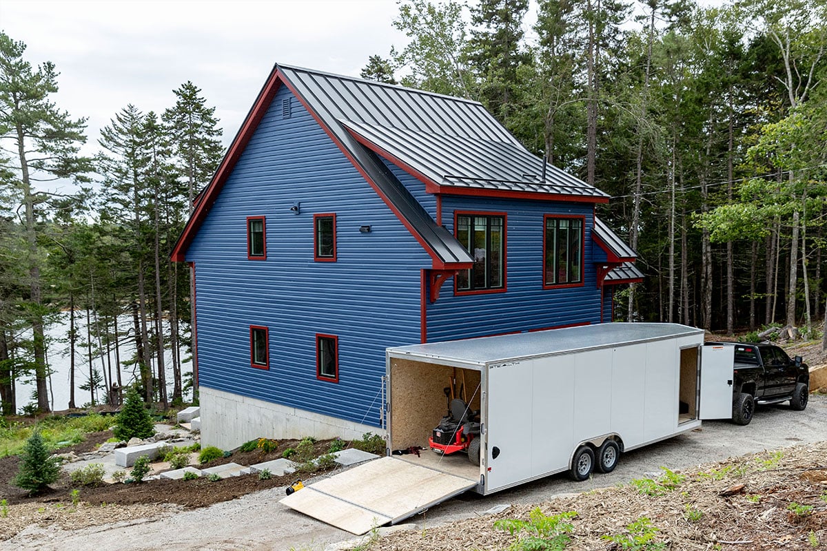 Large enclosed aluminum cargo trailer parked outside a house with rear ramp door open.