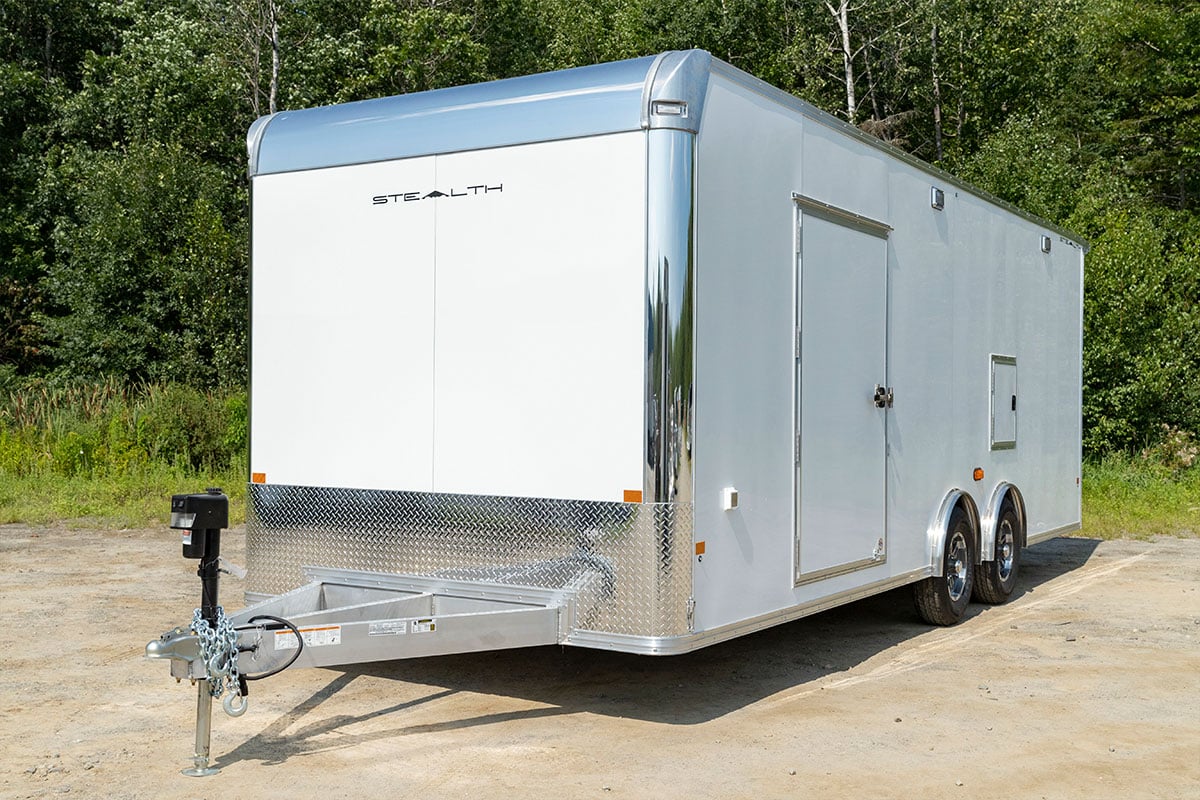 Enclosed flat-front aluminum cargo trailer by ALCOM, parked with doors closed.