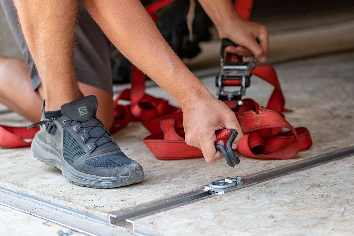 A person is attaching cargo straps to the recessed D-ring in an ALCOM trailer's slide track