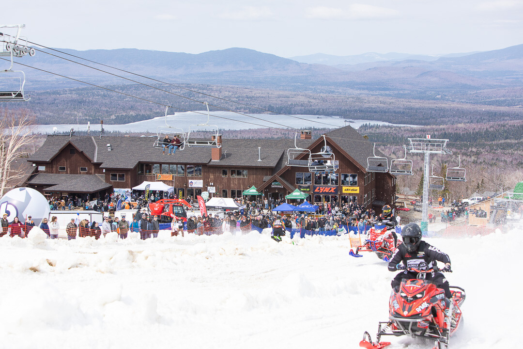 Snowmobile racers riding away from the Saddleback lodge at the 2023 KOTM (Eisenhaur Photography
