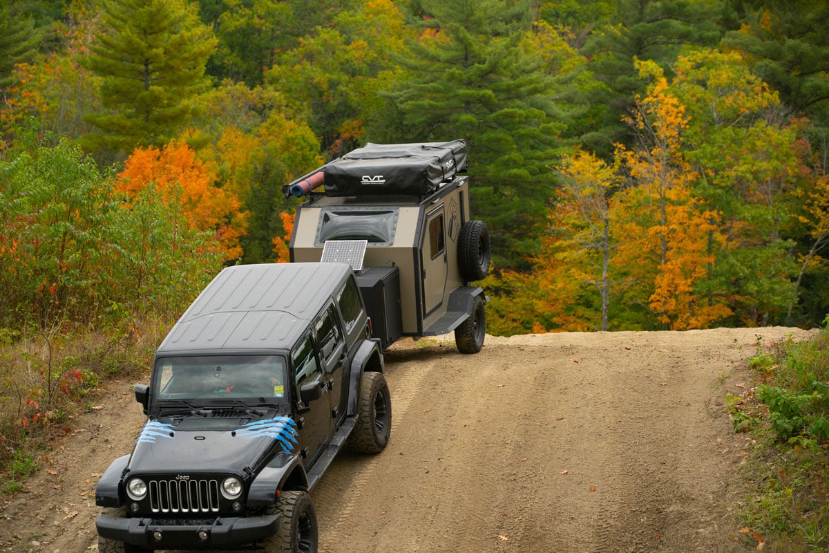 Jeep towing an AO offroad overland camper trailer down a dirt road during fall