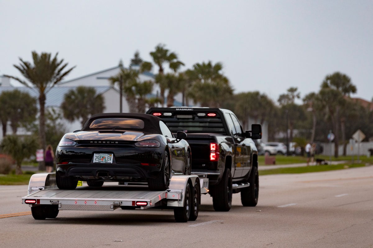 Rear view of a Porsche convertible towed on an open aluminum car hauler by ALCOM in a Florida neighborhood