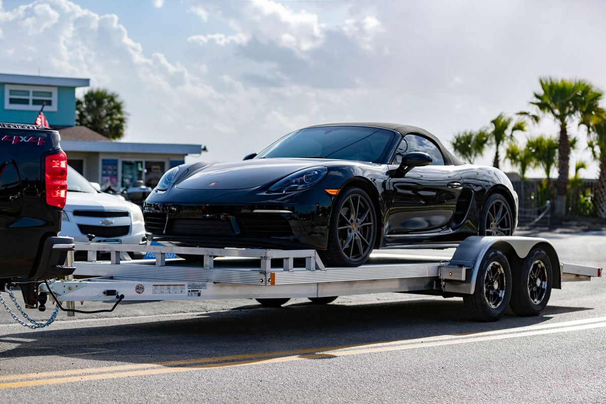Black pickup towing an open aluminum car hauler loaded with a sports car