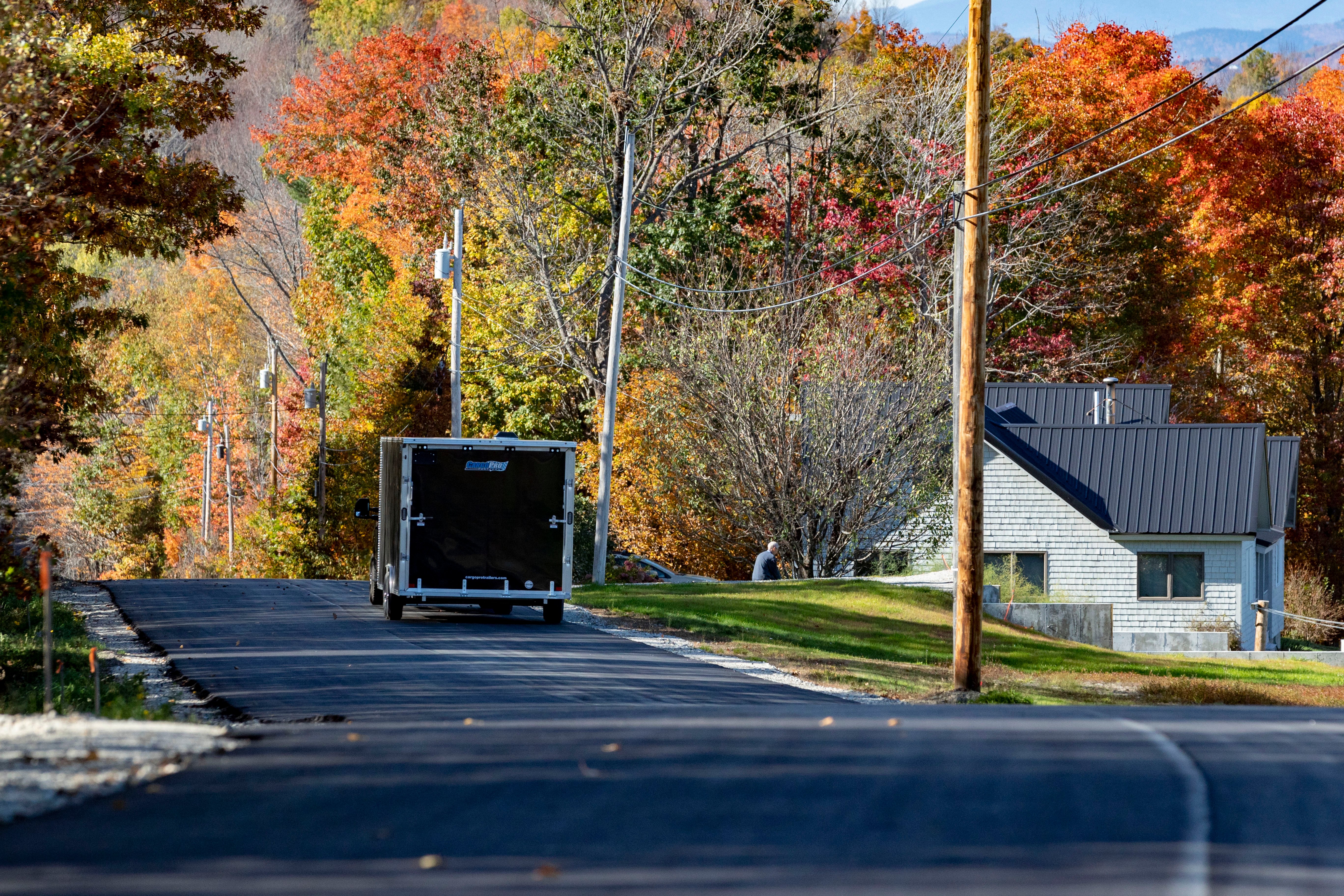 A black pickup truck towing a black enclosed aluminum cargo trailer down a Maine road on a fall day
