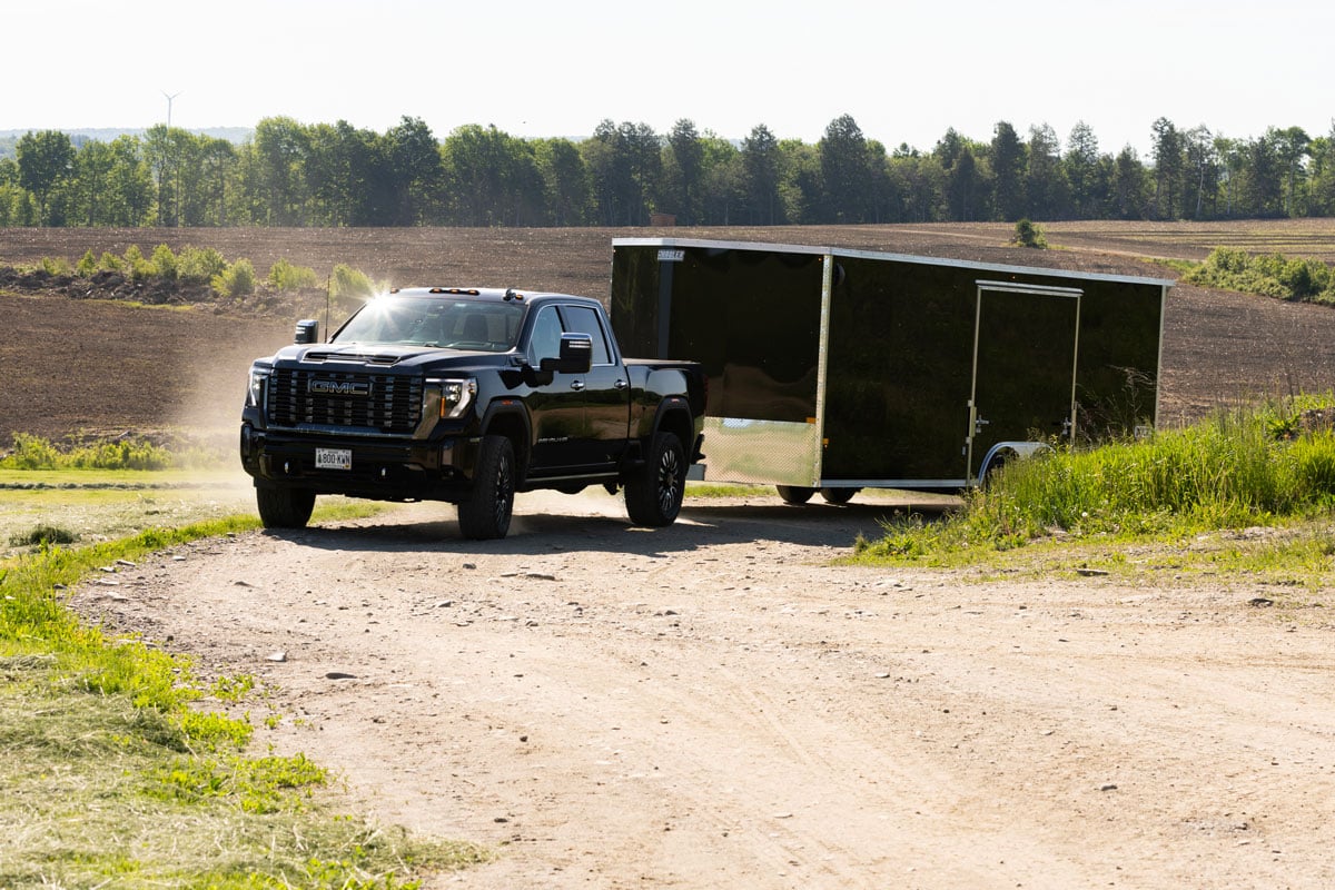 Black pickup truck towing the black XLT Pro car hauler on a dirt road