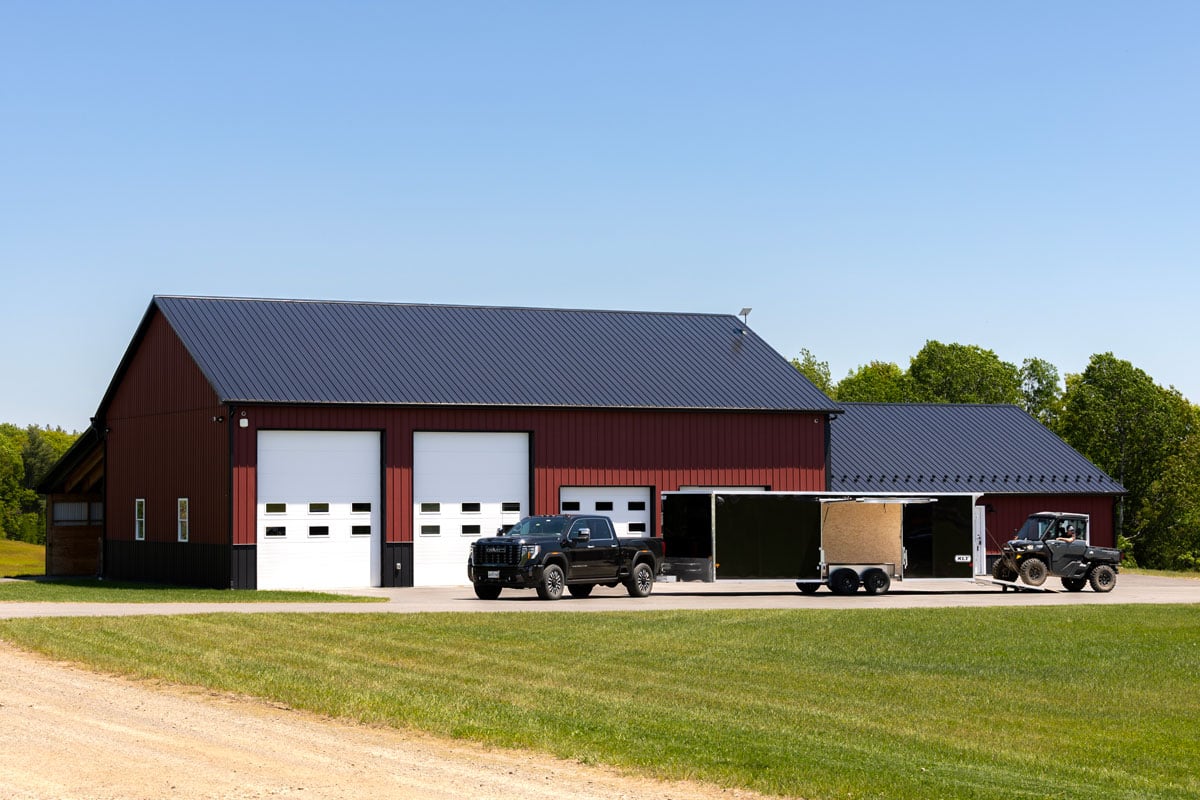 A black pickup and black XLT Pro car hauler parked in front of a red barn with a UTV on the trailer ramp