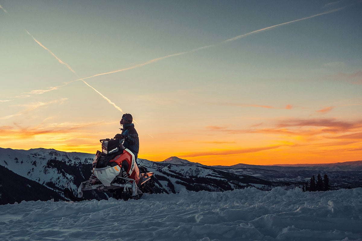 A snowmobiler parked on a scenic mountain overlook; photo by Jamie Fenn
