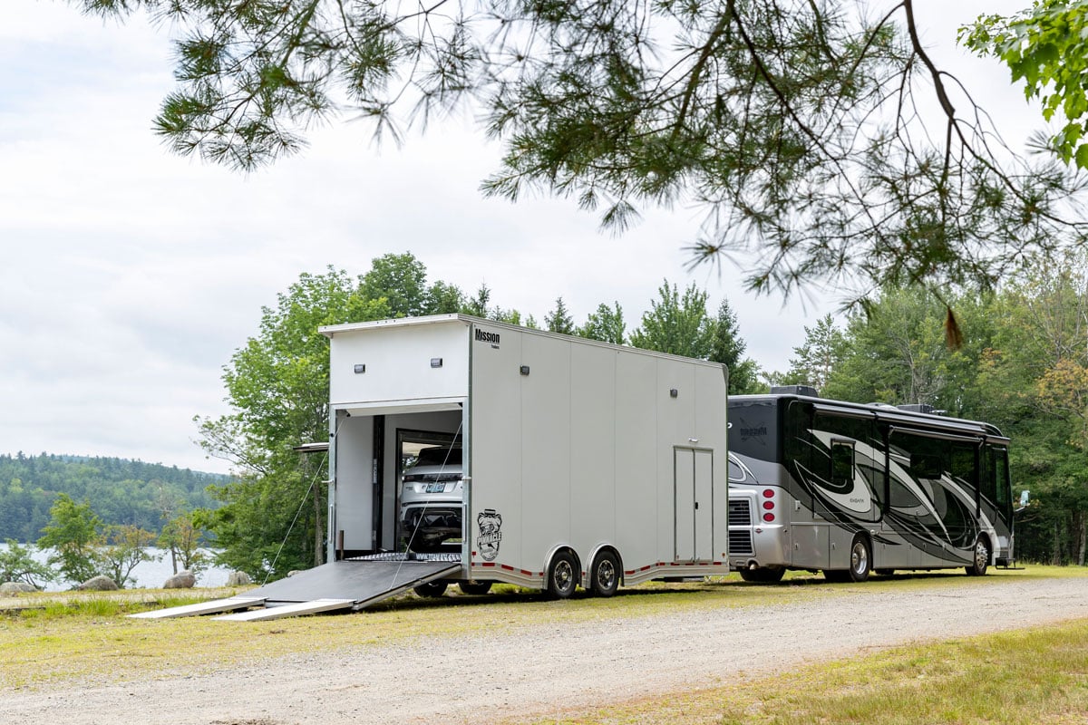 Pinnacle Stacker car hauler trailer with ramp door open, hitched to an RV