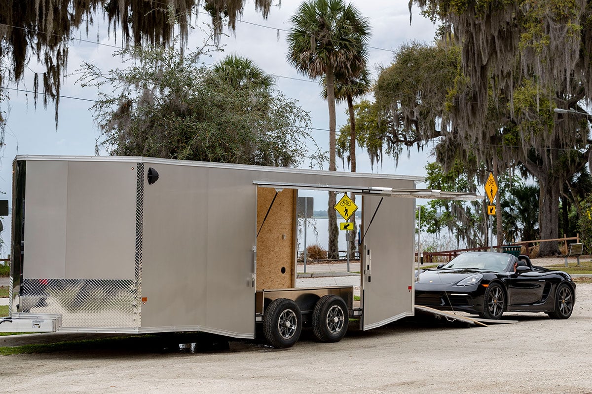 Enclosed car hauler with side escape door open and a sports car ready to load