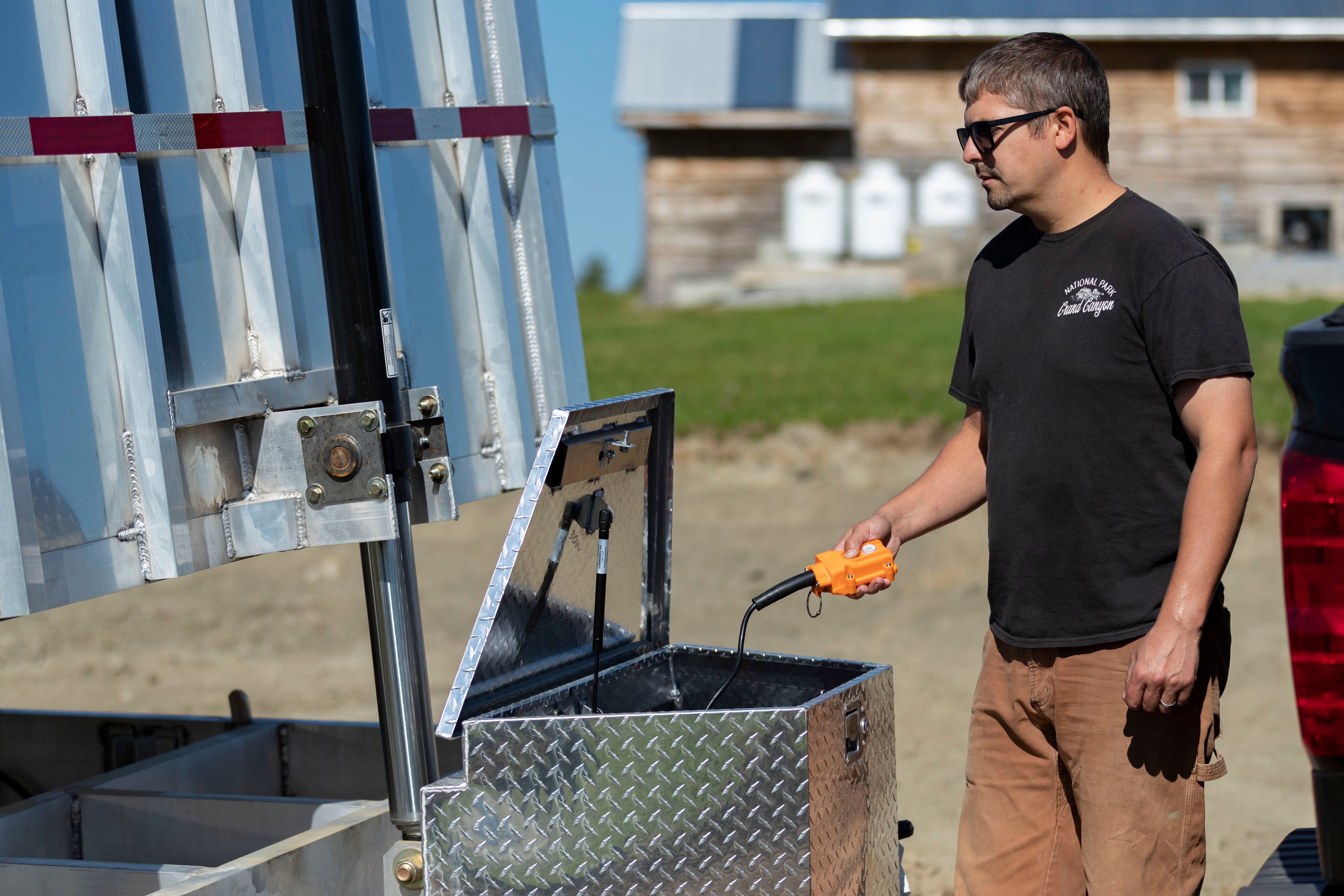 A man using the hoist system on an aluminum dump trailer
