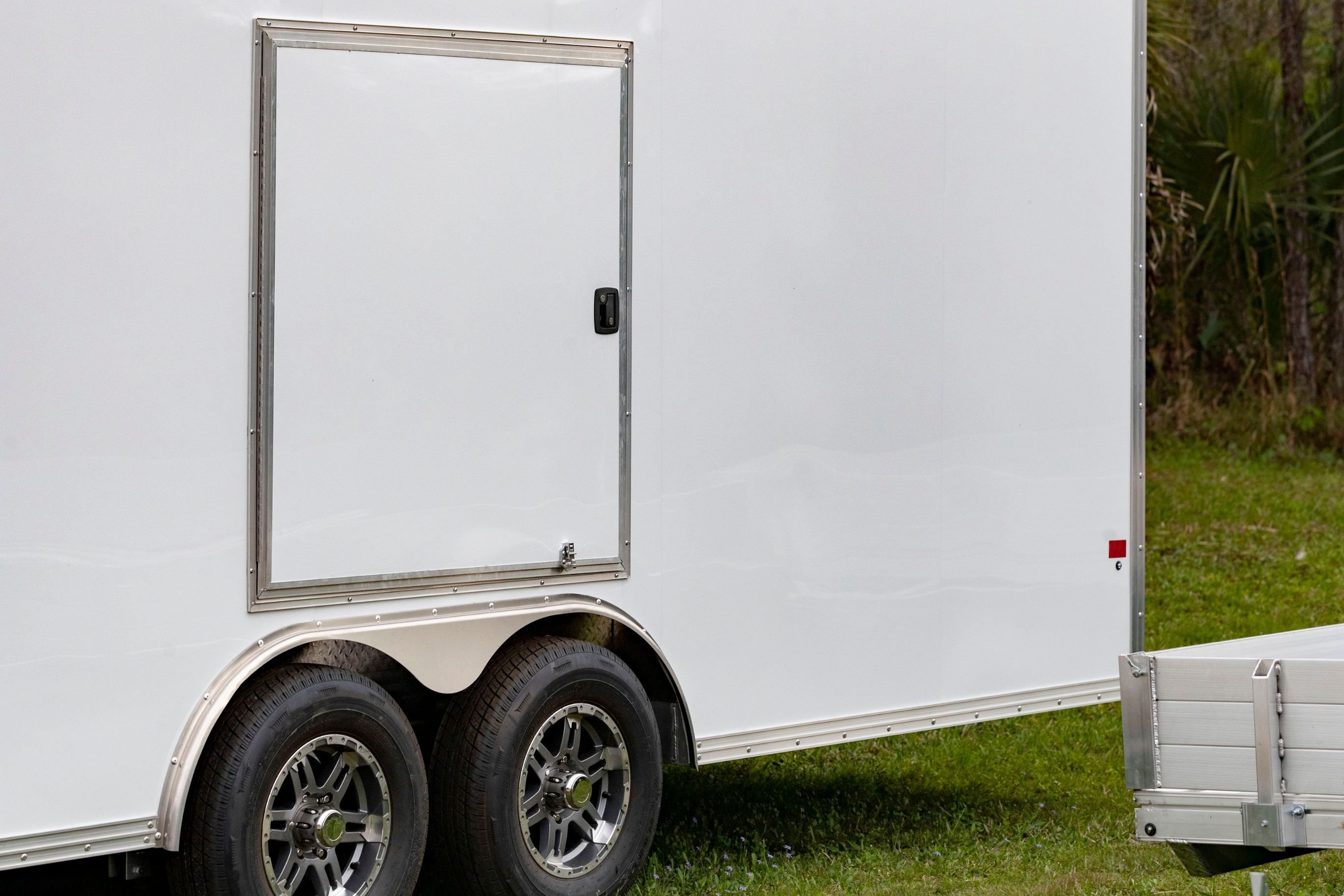 A white cargo trailer with a concession door on the driver's side parked on grass